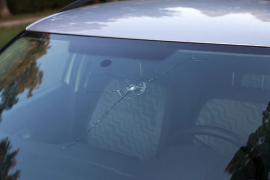 Pare-brise de véhicule endommagé avec impact central et fissures radiales s'étendant sur la surface vitrée